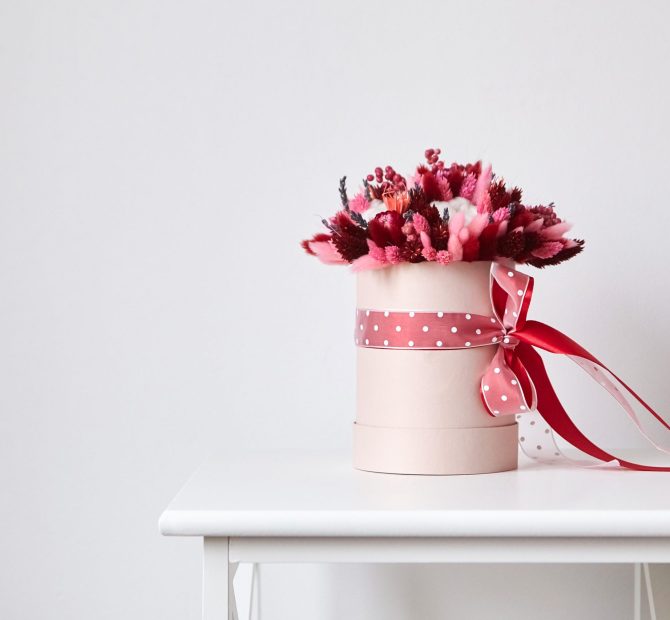 Dried flower bouquet with grasses in pink round hat box in room with white wall